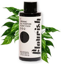 A black bottle of Flourish Organic All-Purpose Plant Food (1 Bottle) by Flourish, featuring a white minimalist label, stands before lush green foliage.