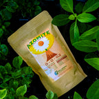 A brown Wellspring Gardens bag of AZOMITE Organic Trace Minerals (from volcanic ash, 14-oz or 2-lb) sits among green plants. The label shows a white flower, volcano image, and notes it’s an organic fertilizer and nutrient additive.