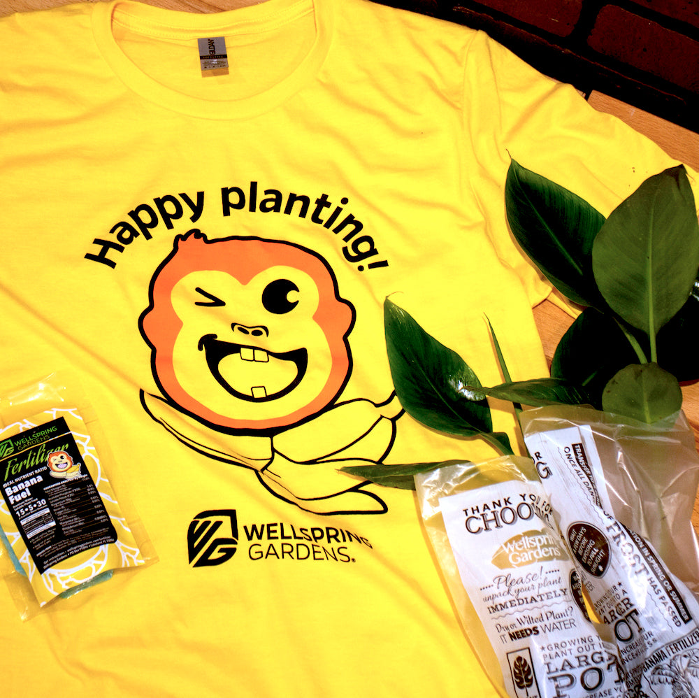 The Mekong Monkey 'Happy planting!' T-shirt by Wellspring Gardens features a bright yellow color, a winking cartoon plant face, cheerful text, and the playful gardening mascot. Perfect for plant lovers!.