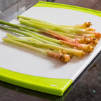 Wellspring Gardens Chinese Keys Galangal Ginger (Fingerroot) - Boesenbergia rotunda, with green stems and pale yellow roots, is displayed on a white cutting board with green edges atop a dark countertop.